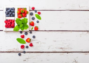 Ahşap arka plan üzerinde beyaz ahşap kutusunda taze ham organik çilek. Metin için yer. Çilek, ahududu, yaban mersini ve nane yaprağı