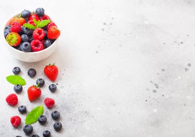 Mutfak Masa arka plan üzerinde beyaz seramik kase taze ham organik çilek. Metin için yer. Çilek, ahududu, yaban mersini ve nane yaprağı