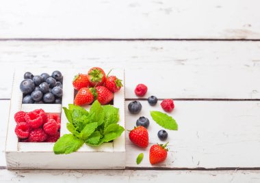 Ahşap arka plan üzerinde beyaz ahşap kutusunda taze ham organik çilek. Metin için yer. Çilek, ahududu, yaban mersini ve nane yaprağı