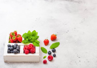 Mutfak Masa arka plan üzerinde beyaz wintage ahşap kutusunda taze ham organik çilek. Metin için yer. Çilek, ahududu, yaban mersini ve nane yaprağı