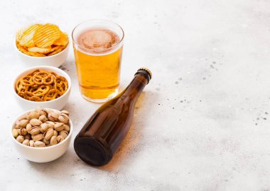 Cam ve zanaat bira şişesini ile taş mutfak arka plan üzerinde yemek saati. Tuzlu kraker ve patates cipsi ve beyaz seramik kase fıstık