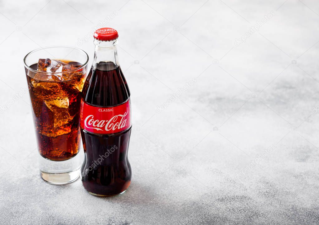 LONDON, UK - SEPTEMBER 28, 2018: Glass and bottle of Coca Cola soda drink with ice cubes and bubbles on stone kitchen background.