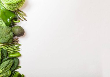 Çeşitli yeşil beyaz arka plan üzerinde ham organik sebze tonda. Avokado, lahana, brokoli, karnabahar ve salatalık ile kesilmiş ve gevşek mung fasulye, pak choi, biber ve marul