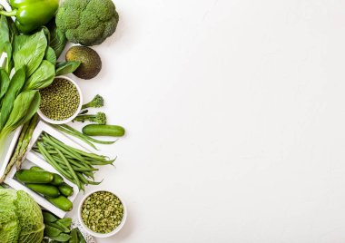 Çeşitli yeşil beyaz arka plan üzerinde ham organik sebze tonda. Avokado, lahana, brokoli, karnabahar ve salatalık ile kesilmiş mung fasulye ve bezelye beyaz kase. 