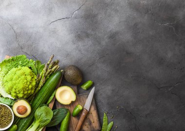 Çeşitli yeşil koyu taş zemin üzerine ahşap kutusunda ham organik sebze tonda. Avokado, lahana, karnabahar ve salatalık ile kesilmiş fasulye ve bıçak ile kesme tahtası.