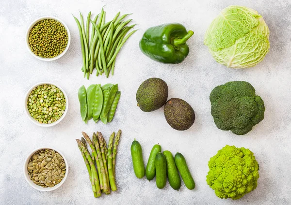 Assorted green toned raw organic vegetables on white background. Avocado, cabbage, broccoli, cauliflower and cucumber with trimmed and mung beans, pak choi, loose pepper and lettuce