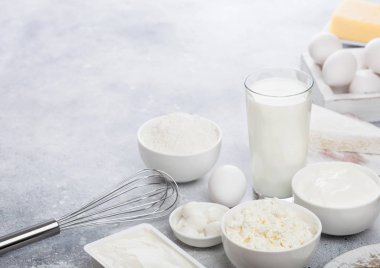 Beyaz masa arka planında taze süt ürünleri. Bir bardak süt, bir kase ekşi krema, süzme peynir, un ve mozzarella. Yumurta ve peynir. Çelik çırpıcı