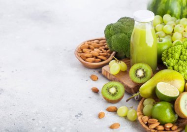 Cam şişe taze yüzlü suyu organik yeşil tonda meyve ve sebze taş mutfak masa arka plan üzerinde. Badem fındık ile kase.