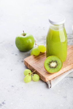 Taş zemin üzerine organik yeşil tonda meyve suyuyla taze yüzlü bir cam şişe. Elma, kivi ve üzüm