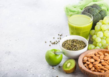 Bardak taze yüzlü suyu organik yeşil tonda meyve ve sebze taş mutfak masa arka plan üzerinde. Badem fındık ile kase.