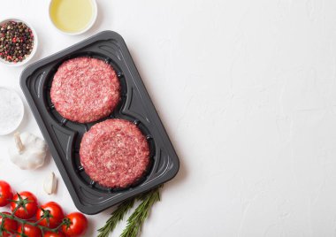 Plastik tepsi ile baharat ve otlar ile çiğ kıyılmış ev yapımı ızgara sığır eti hamburger. Üstten görünüm ve metin için yer.