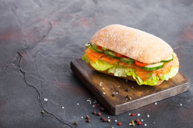 Marul ve salatalığın üzerinde siyah taş zemin üzerine vintage Doğrama tahtası ile taze sağlıklı somon sandviç. Kahvaltı snack