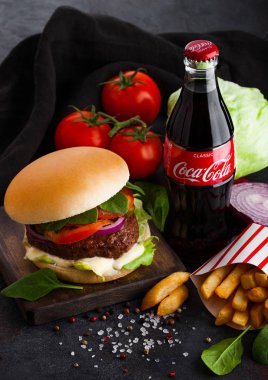 Londra, İngiltere - 05 Ekim 2018: Şişe Coca Cola meşrubat taze sığır eti hamburger ve patates kızartması ile tabloda koyu arka plan üzerinde sebzeli.
