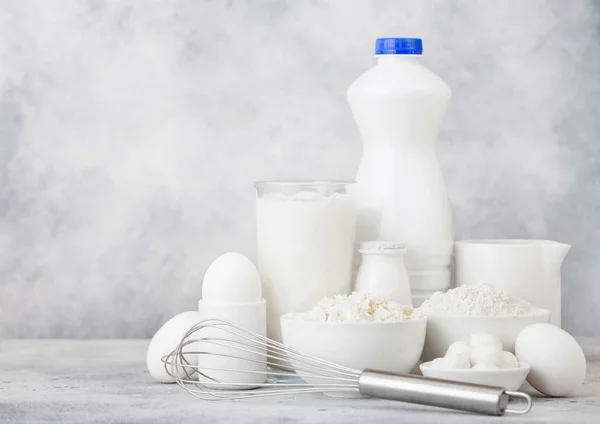 Fresh dairy products on white background. Glass jar of milk, bowl of sour cream, cottage cheese and baking flour and mozzarella. Eggs and cheese. Steel whisk