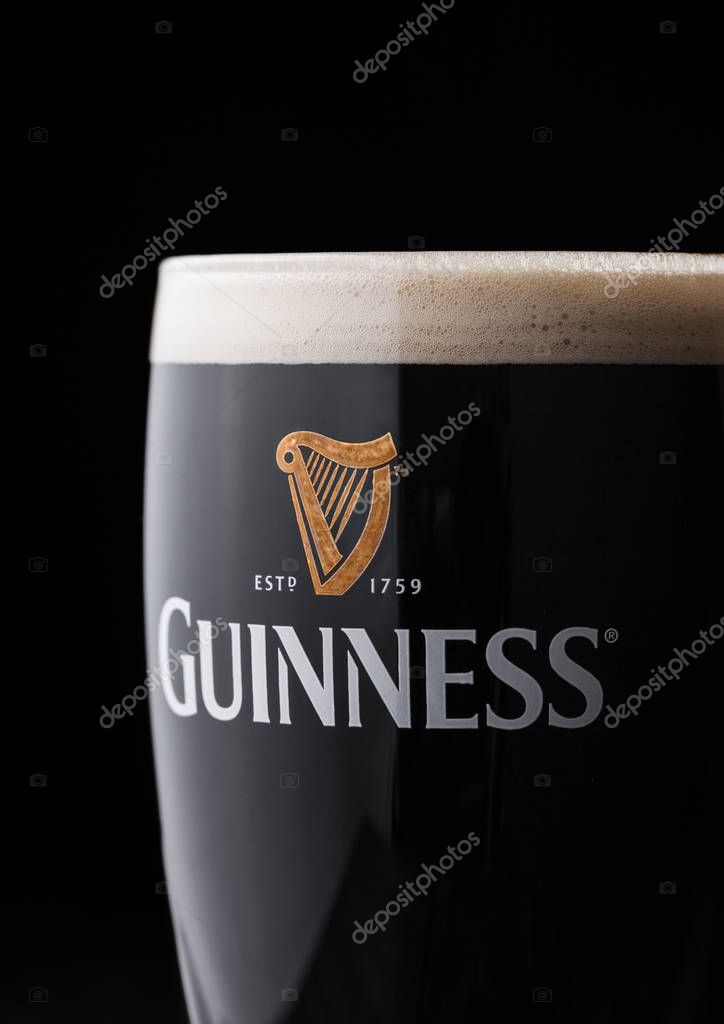 LONDON, UK - APRIL 27, 2018: Original glass of Guinness draught stout beer on top of old wooden barrel. Guinness beer has been produced since 1759 in Dublin, Ireland.