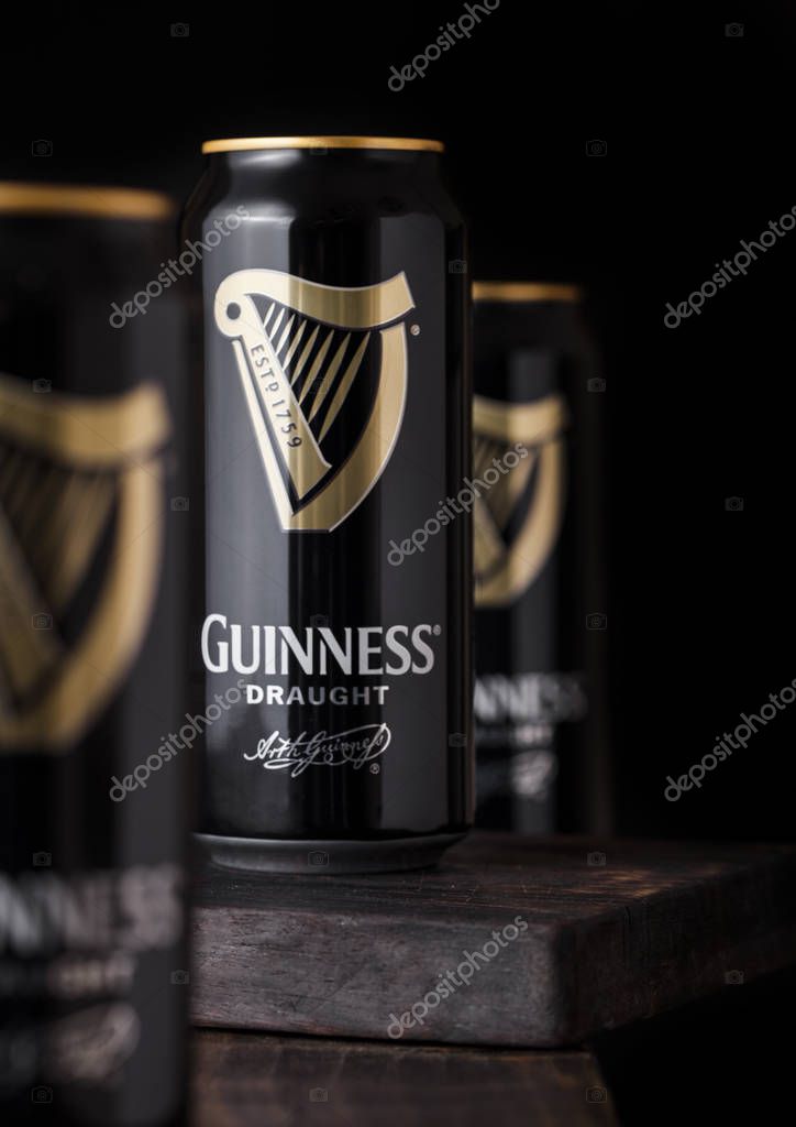 LONDON, UK - APRIL 27, 2018: Aluminium cans of Guinness draught stout beer bottle on dark wooden background. Guinness beer has been produced since 1759 in Dublin, Ireland.