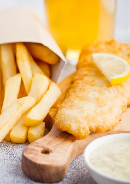 Geleneksel İngiliz balık ve cips tartar sosu abd cam Doğrama Kurulu üzerinde üzerinde zanaat lager bira ile taş arka plan beyaz.