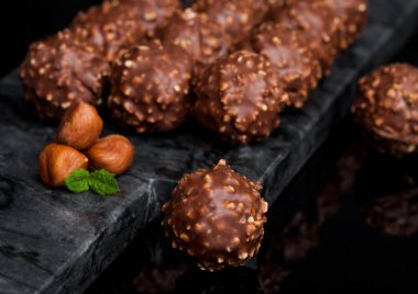 Fındık parçaları ve siyah mermer zemin üzerine nane yaprağı ile lüks çikolata şekerleme.