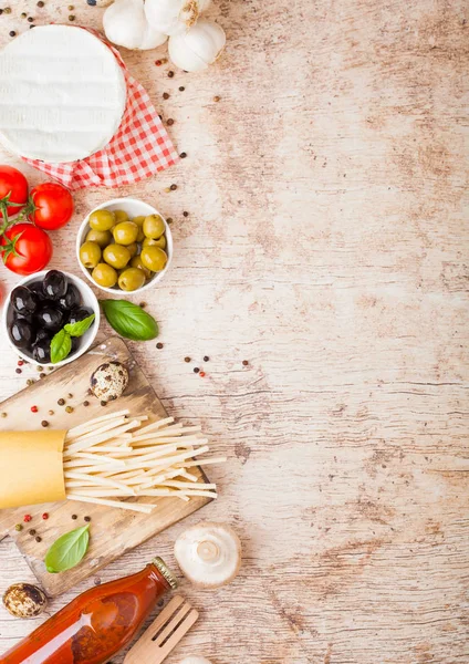 Homemade spaghetti pasta with quail eggs with bottle of tomato sauce and cheese on wood background. Classic italian village food. Garlic, champignons, black and green olives, oil and spatula