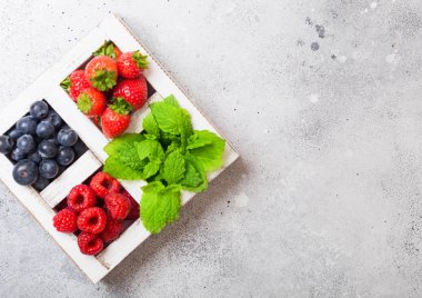 Mutfak Masa arka plan üzerinde beyaz wintage ahşap kutusunda taze ham organik çilek. Metin için yer. Çilek, ahududu, yaban mersini ve nane yaprağı