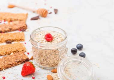 Çilek tatlım kaşık ve yulaf mermer masa arka plan üzerinde kavanoz ile organik tahıl granola bar. Üstten görünüm. Çilek, ahududu ve badem fındık ile yaban mersini.