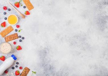 Çilek tatlım kaşık ve taş zemin üzerine süt İçecek şişe ve kavanoz yulaf ile organik tahıl granola bar. Üstten görünüm. Çilek, ahududu ve badem fındık ile yaban mersini.