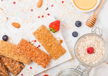 Çilek tatlım kaşık ve yulaf kavanoz ile mermer tahtada ve mermer masa arka plan üzerine Hindistan cevizi ile organik tahıl granola bar.