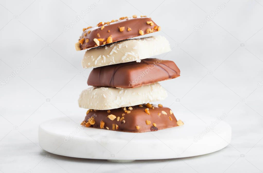 Luxury belgian chocolate and coconut cookies selection on marble coasters and kitchen table background.