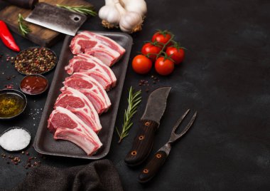 Taze çiğ kasapların vintage et balta ile plastik tepsi ve çatal bıçak siyah arka plan üzerine ile Dana pirzola kuzu. Tuz, biber, domates ve sarımsak.