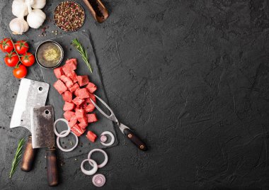 Ham yalın güveç dana domuz biftek vintage et balta ve çatal ile taş zemin üzerine doğranmış. Tuz ve karabiber taze biberiye, kırmızı soğan ve sarımsak ile.