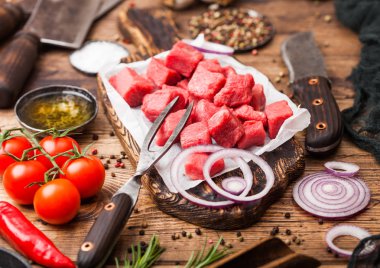 Ham yalın güveç dana domuz biftek vintage et balta ve bıçak ve çatal ile ahşap arka plan üzerine doğranmış. Tuz ve karabiber taze biberiye, kırmızı soğan ve sarımsak ile.