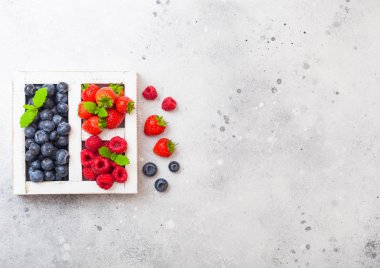 Mutfak Masa arka plan üzerinde beyaz wintage ahşap kutusunda taze ham organik çilek. Metin için yer. Çilek, ahududu, yaban mersini ve nane yaprağı