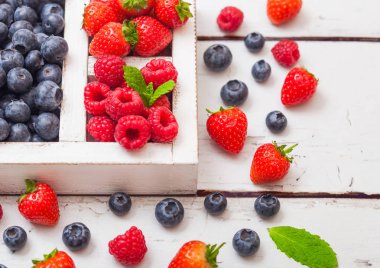 Ahşap arka plan üzerinde beyaz ahşap kutusunda taze ham organik çilek. Yakın çekim. Çilek, ahududu, yaban mersini ve nane yaprağı