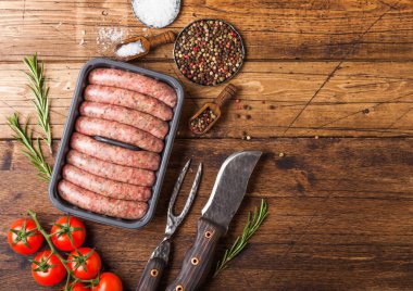 Ham sığır eti ve domuz sosis vintage bıçak ve çatal ahşap arka plan üzerinde plastik tepsi. Tuz ve karabiber biberiye ve domates ile.