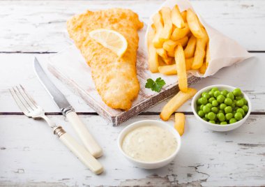 Geleneksel İngiliz balık ve cips tartar sosu çatal ve bıçak ve yeşil bezelye ile Doğrama Kurulu Tarih ile ahşap arka plan beyaz.