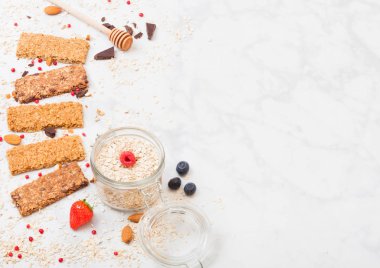 Çilek tatlım kaşık ve yulaf mermer masa arka plan üzerinde kavanoz ile organik tahıl granola bar. Üstten görünüm. Çilek, ahududu ve badem fındık ile yaban mersini.