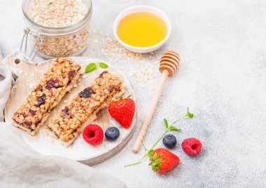 Organik tahıl granola bar üzerinde çilek ile vintage tahta kaşık bal ve yulaf mermer zemin üzerine kavanoz ile yuvarlak. Çilek, ahududu ve nane yaprağı ile yaban mersini 