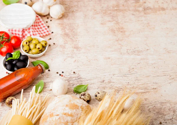 Homemade spaghetti pasta with quail eggs with bottle of tomato sauce and cheese on wood background. Classic italian village food. Garlic, champignons, black and green olives, oil and bread.