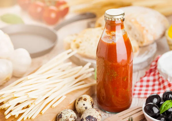 Homemade spaghetti pasta with quail eggs with bottle of tomato sauce and cheese on wooden background. Classic italian village food. Garlic, black and green olives, oil and bread.