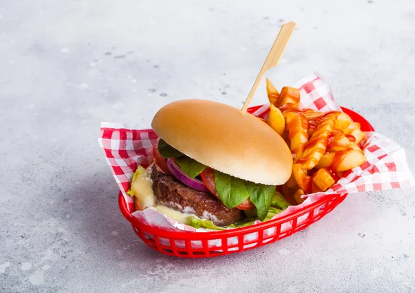 Fresh beef burger with sauce and vegetables with potato chips fries in red serving basket on stone kitchen table background.