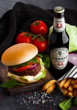 Londra, İngiltere - 05 Ekim 2018: Şişe Guinness özgün bira taze sığır eti hamburger ve patates kızartması ile tabloda koyu arka plan üzerinde sebzeli.