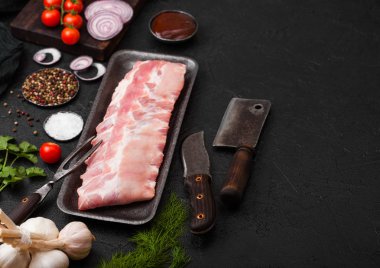 Plastik tepsi çiğ Domuz kaburga ve vintage bıçak ve çatal siyah taş zemin üzerine. Taze domates ve kırmızı soğan sarımsak tuz ve biber ve taze dereotu