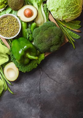 Çeşitli yeşil koyu arka plan üzerinde ham organik sebze tonda. Avokado, lahana, brokoli, karnabahar ve salatalık kesilmiş fasulye ile.
