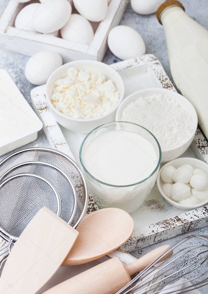 Fresh dairy products on white table background. Glass of milk, bowl of flour and cottage cheese and eggs. Box of baking utensils. whisk and spatula in vintage wooden box.