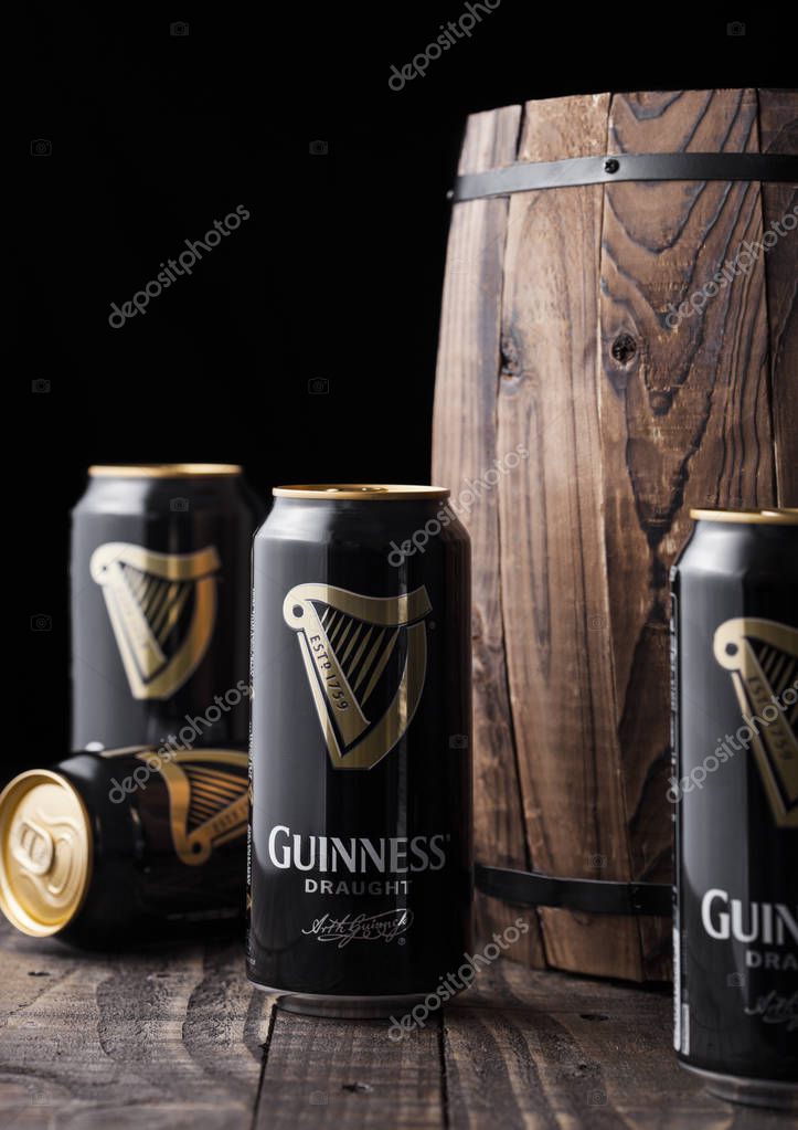 LONDON, UK - FEBRUARY 06, 2019: Aluminium cans of Guinness draught stout beer  next to old wooden barrel. Guinness beer has been produced since 1759 in Dublin, Ireland.