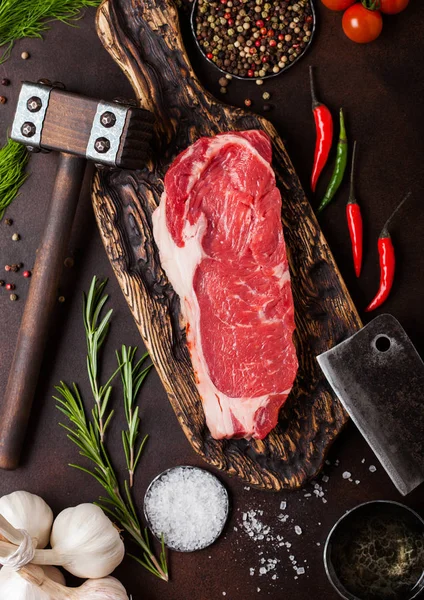 Raw sirloin beef steak on old chopping board with salt and pepper and vintage meat hatchets and hammer on rusty background.Red pepper, tomatoes and garlic. — Stock Photo, Image