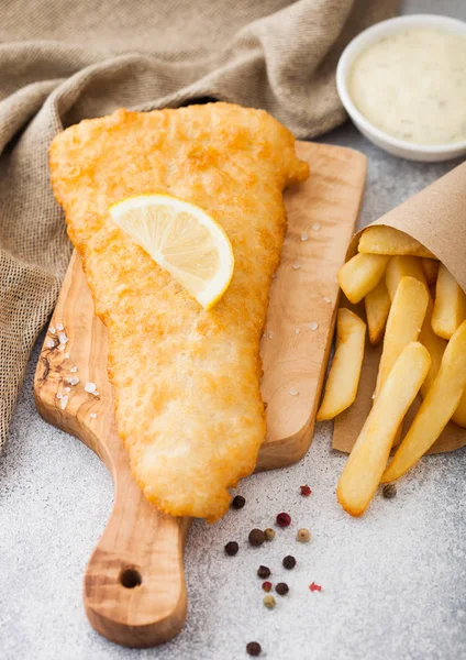 Pescado británico tradicional y patatas fritas con salsa tártara sobre tabla de cortar con toalla de lino sobre fondo de mesa de piedra blanca . — Foto de Stock