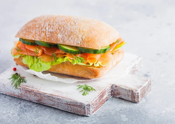 Marul ve salatalığın üzerinde vintage doğrama tahtası beyaz taş zemin üzerine taze sağlıklı somon sandviç. Kahvaltı snack. Diyet gıda — Stok fotoğraf