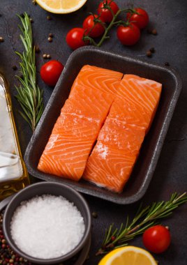 Plastik kap taze somon dilimi yağ domates ve limon taş mutfak arka plan ile. Biberiye ve tuz ile