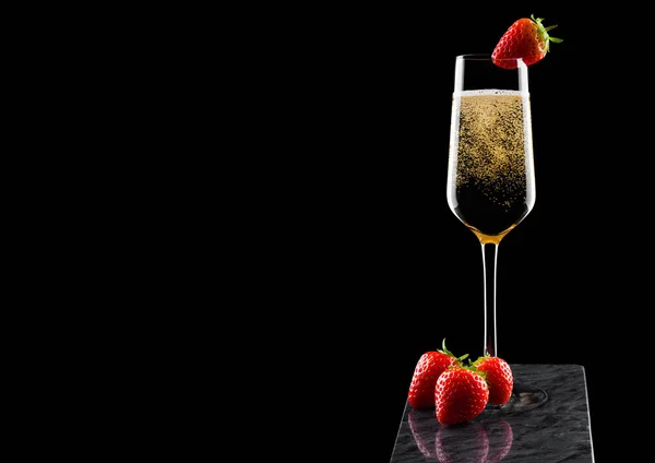 Elegante copa de champán amarillo con fresa en la parte superior y bayas frescas en tablero de mármol negro sobre fondo negro. Espacio para texto —  Fotos de Stock